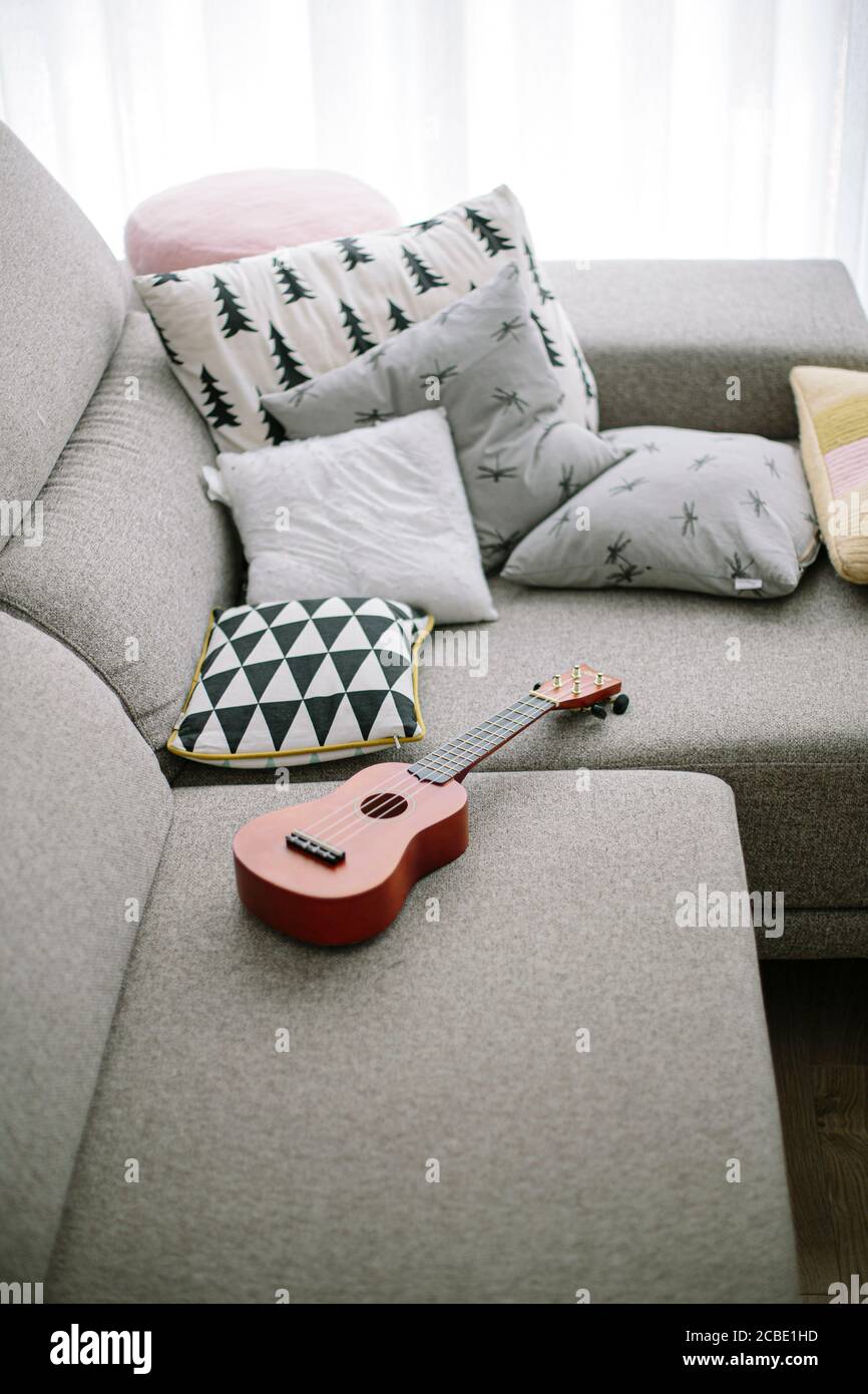 Winziges braunes Ukulele Musikinstrument auf einem grauen Sofa mit Kissen zu Hause Stockfoto