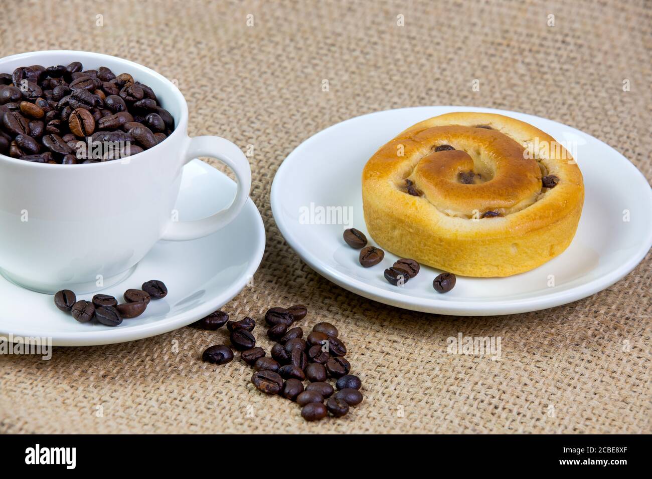 tasse mit geröstet Kaffeebohnen und Kuchen auf Jute Tischdecke Stockfoto