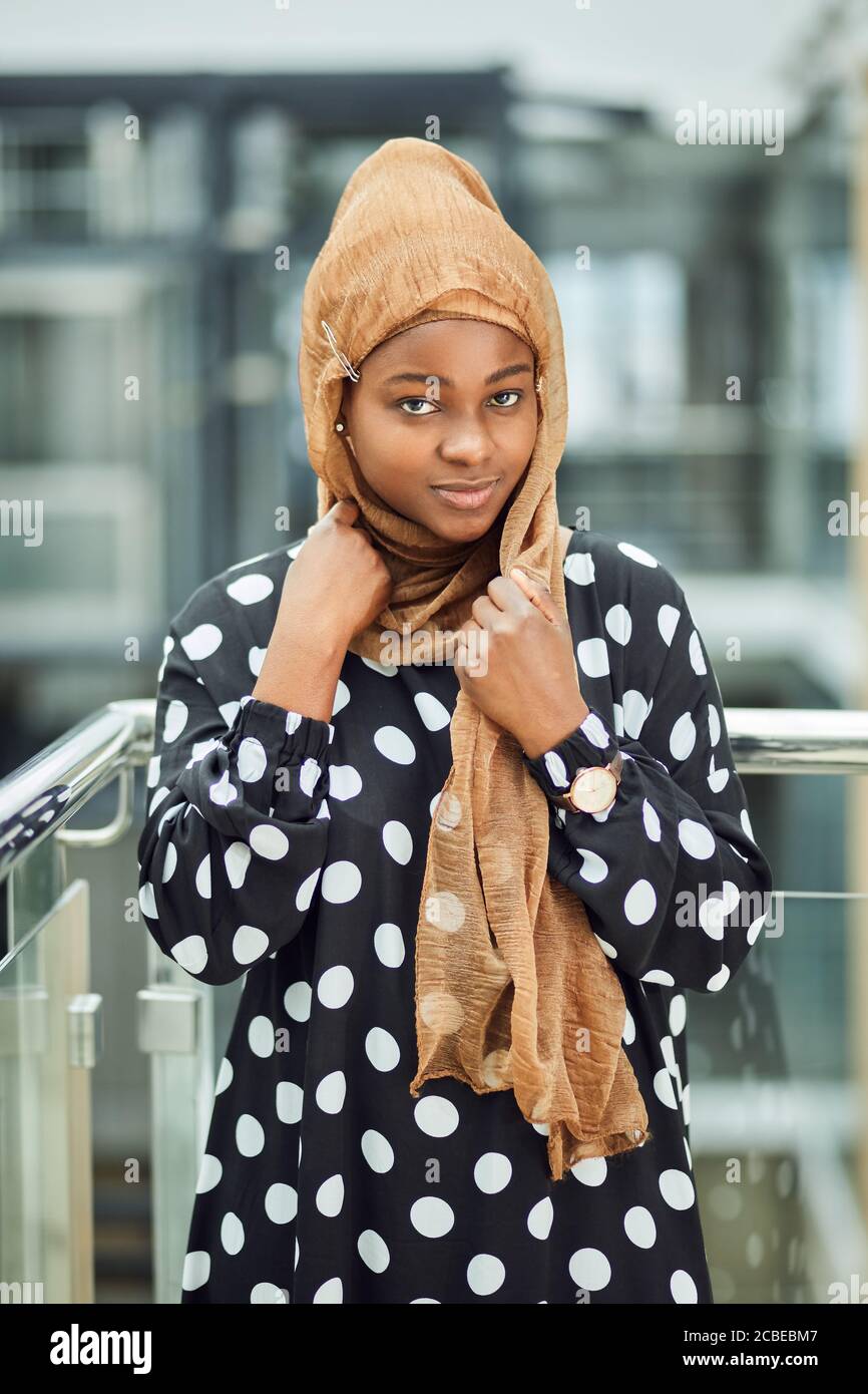 Schöne junge afrikanische muslimische Frau in modischen islamischen Outfit in Urbane Umgebung lächelt an der Kamera Stockfoto