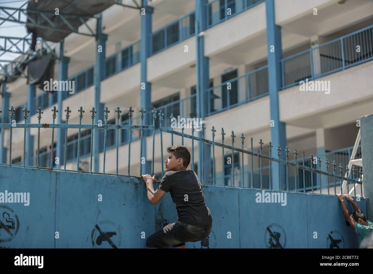 Al-Shati, Palästinensische Gebiete. August 2020. Palästinensische Studenten erklimmen das Tor einer Schule, die vom Hilfswerk der Vereinten Nationen für Palästina-Flüchtlinge (UNRWA) im Flüchtlingslager Al-Shati betrieben wird, um einen Blick auf den Schaden zu werfen, der durch eine Rakete verursacht wurde, die angeblich von einem israelischen Flugzeug am frühen Donnerstag abgeworfen wurde, während sie über Nacht Hamas-Ziele aufschlagen In Gaza als Reaktion auf Brandballons, die aus dem Gazastreifen nach Südisrael geschossen wurden. Kredit: Mohammed Talatene/dpa/Alamy Live Nachrichten Stockfoto