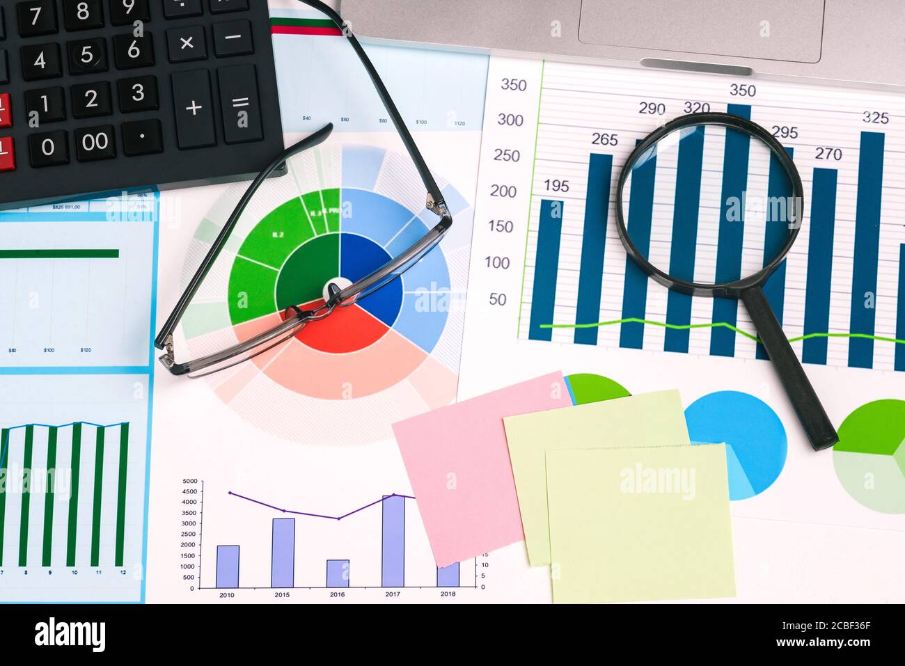 Lupe, Brille, Taschenrechner und Haftnotizen auf Ihrem Desktop. Statistische Diagramme mit Zahlen. Finanzdokumente mit kommerziellen Daten Stockfoto