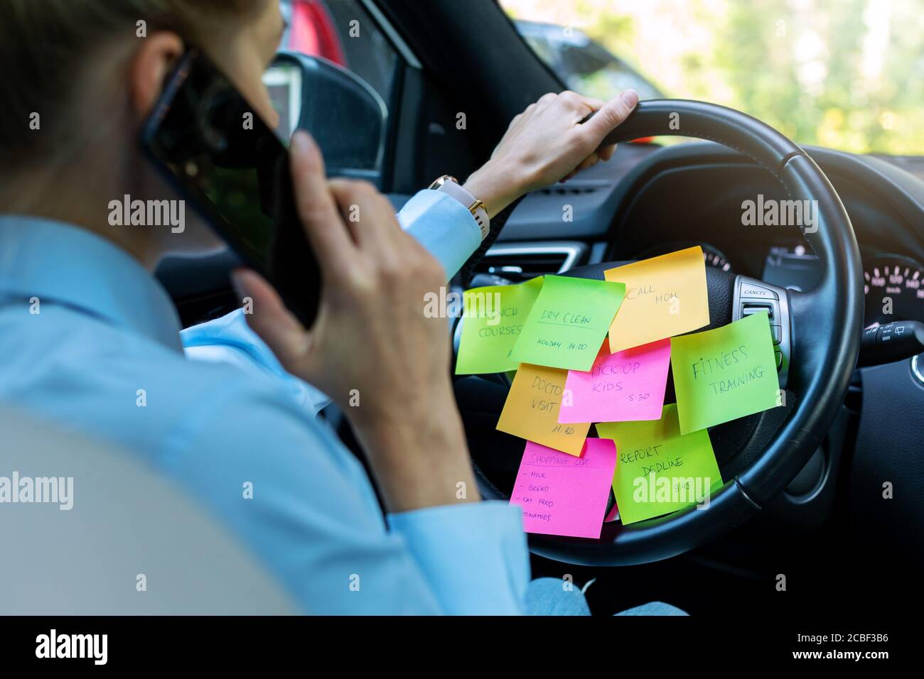 Konzept des vollen Tagesplanens - Frau, die mit dem Auto fährt Listen Sie Notizen auf dem Rad auf und sprechen Sie auf dem Telefon Stockfoto