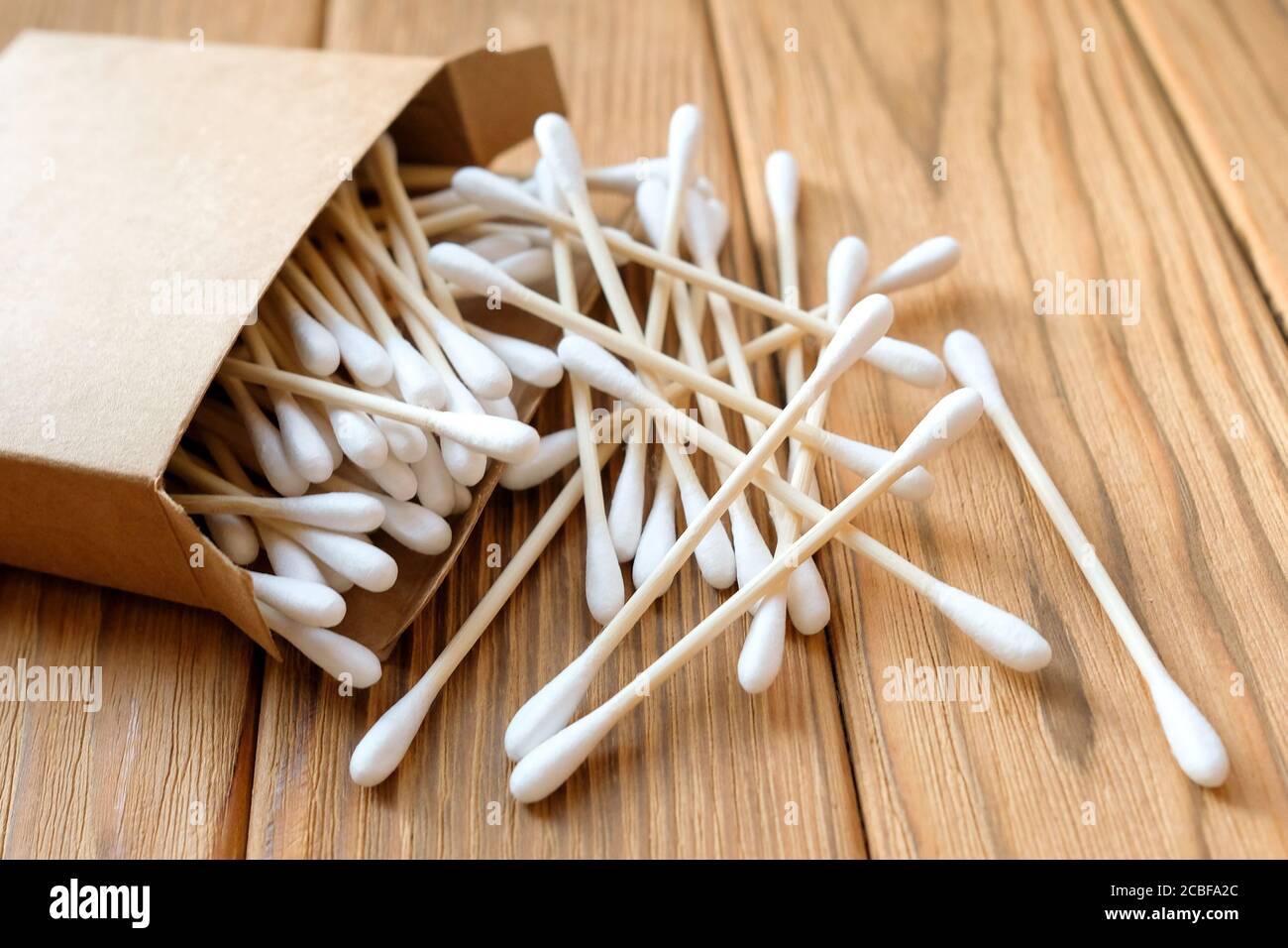 Baumwollknospen sind auf einem hölzernen Hintergrund verstreut. Umweltfreundliche Ohrenstöpsel aus Baumwolle. Stockfoto