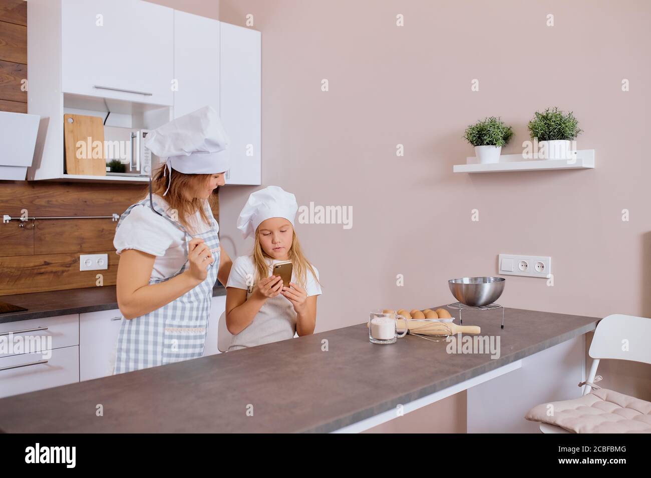 kaukasische Mutter und Tochter stehen zusammen Blick auf Smartphone, auf der Suche nach delicipus Rezept der Kuchen, auf der Suche, Tragen Schürze Stockfoto