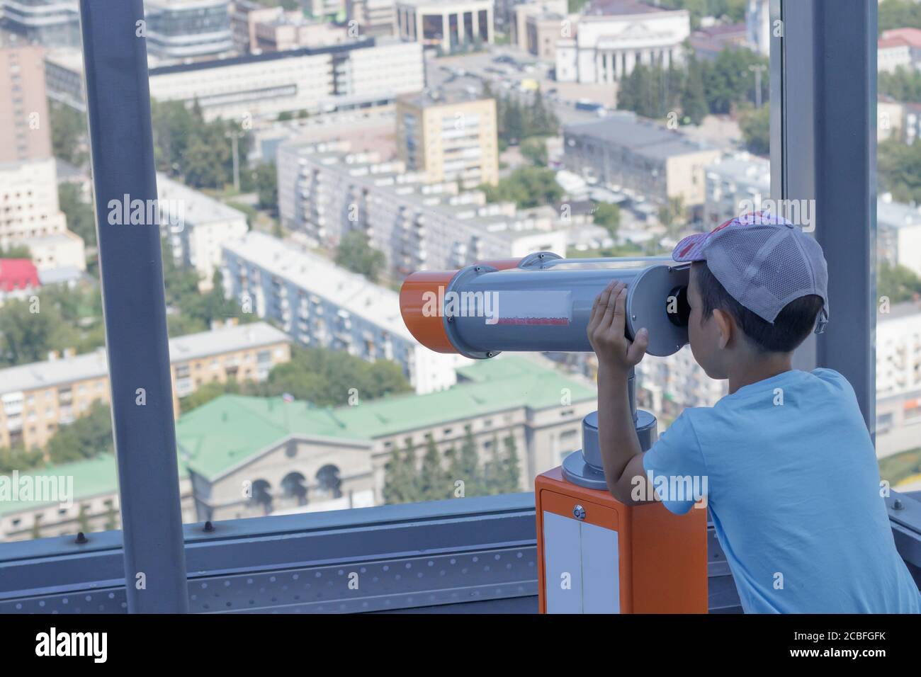 Der Junge blickt aus einem Panoramafenster eines Hochhauses auf der Stadt Jekaterinburg, Russland, in ein Teleskop Stockfoto