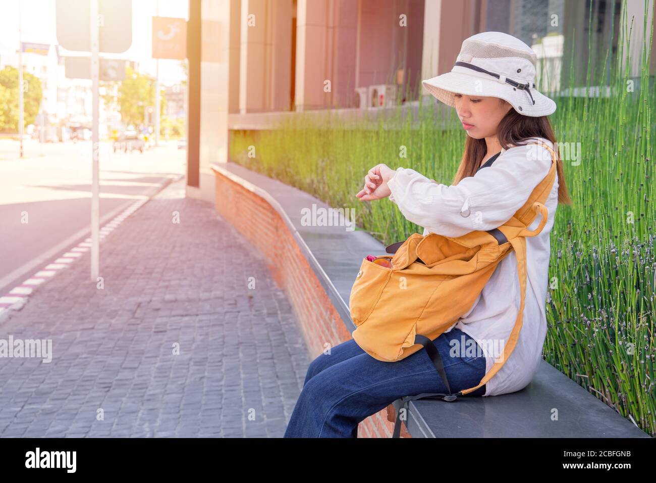 Asiatische Touristen warten suchen Armbanduhr für die Überprüfung der Zeit und Sorgenausdruck für einen Freund, der draußen auf der Straße sitzt Stockfoto