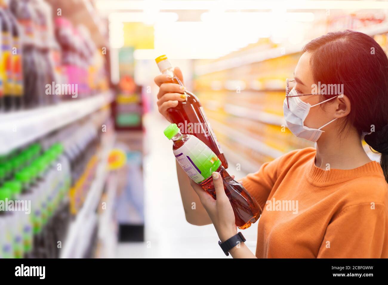 Asiatische Kunden einkaufen im Supermarkt mit Gesichtsmaske Wahl wählen Und vergleichen Fischsauce durch Lesen der Produkte Detail Etikett auf Regal Stockfoto