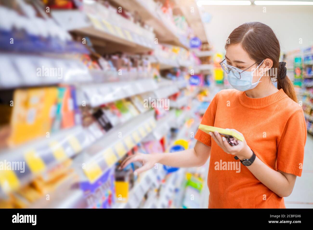 Asiatische Frau trägt Gesichtsmaske für gesundes Gehen bei Shopping Mart Wahl Produkte im Supermarkt Regal. Stockfoto