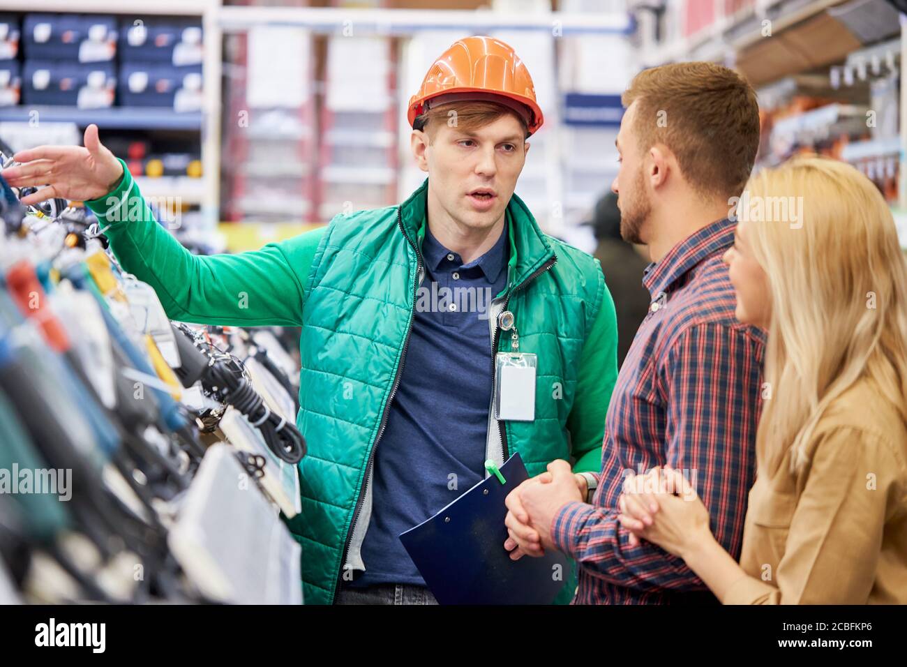 Affable kaukasischen männlichen Lagerarbeiter beraten und helfen Kunden, zeigen die beste Variante des Produkts auf Lager, verheiratetes Paar Fragen stellen, intere Stockfoto