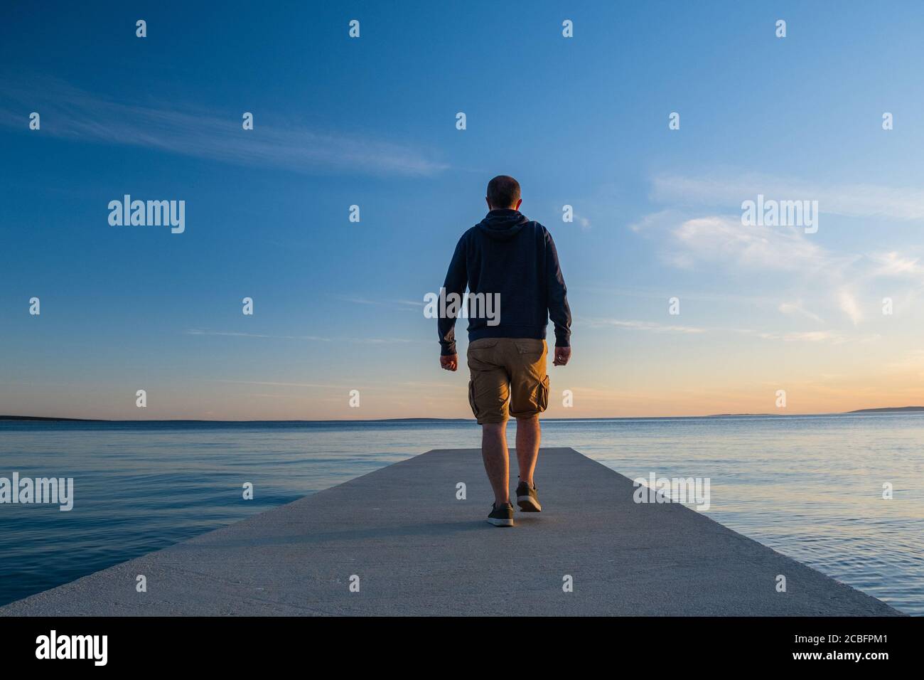 Mann, der auf einem langen Dock steht und den Horizont des Meeres bei Sonnenuntergang, Insel von Pag, Adria, Kroatien, Gedanken-Konzept beobachtet Stockfoto