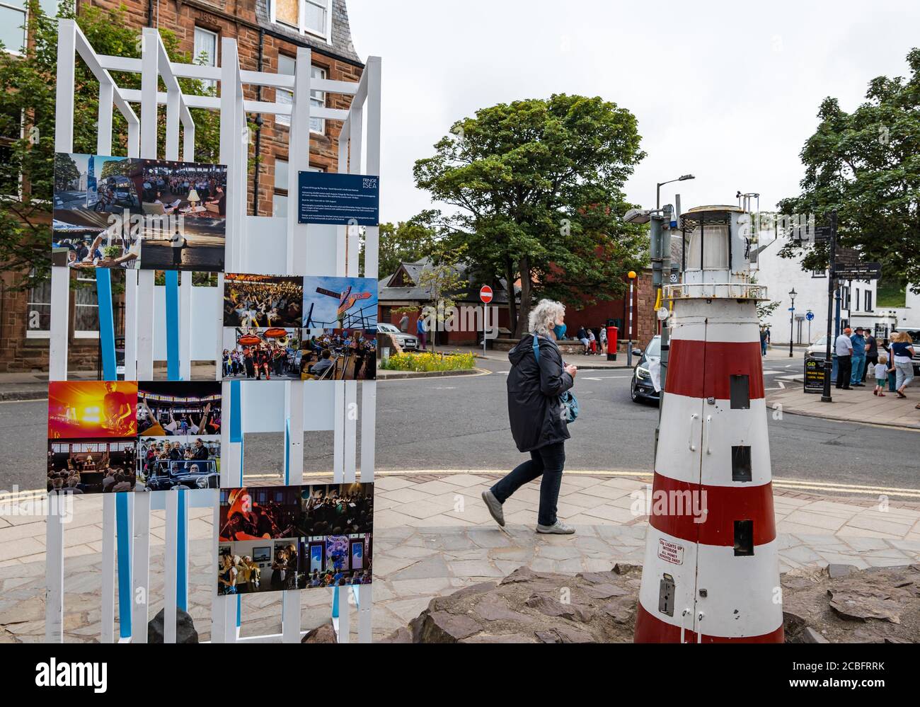 North Berwick, East Lothian, Schottland, Großbritannien, 13. August 2020. Covid-19 Effects: Eine Ausstellung von Fotografien früherer Fringe-by-the-Sea erinnert an die Absage des diesjährigen Festivals, das im Moment stattfand, als eine ältere Frau mit Gesichtsmaske vorbeispaziert Stockfoto