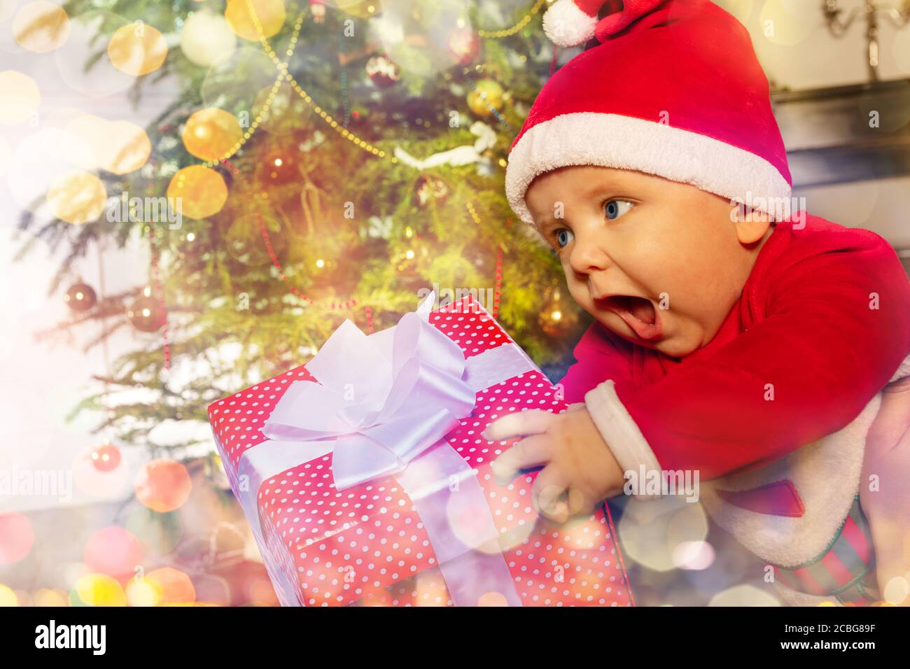 Happy Little Kleinkind Baby junge mit Schrei halten Neujahr Geschenk vor dem Weihnachtsbaum Stockfoto