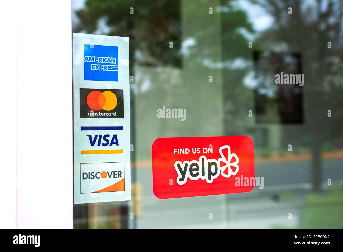 Mastercard, VISA, American Express, Discover Zahlungsoptionen, die an der Restauranttür angepriesen werden. Ein roter Aufkleber Aufkleber fördert Yelp Crowdsourcing Bewertungen Stockfoto