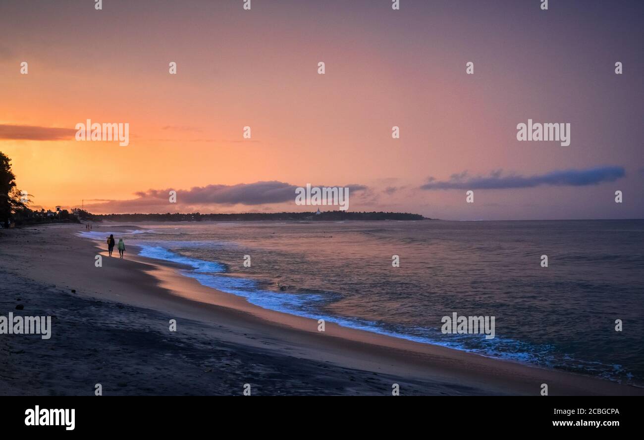 Leute, die am Strand spazieren gehen. Schöner Sonnenuntergang über dem Meer, oranger Himmel. Arugam Bay, Ceylon Stockfoto
