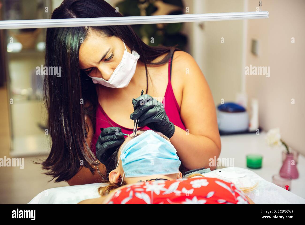 Frau setzen falsche Wimpern, um Dame im Schönheitssalon mit Masken, neue normale Stockfoto