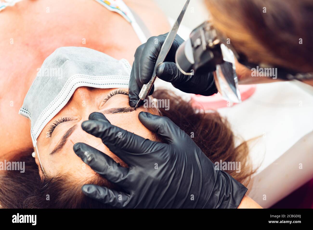 Kosmetikerin in Beauty-Center Durchführung einer Augenbraue Behandlung an Kunden, mit Masken während der neuen Normalität Stockfoto