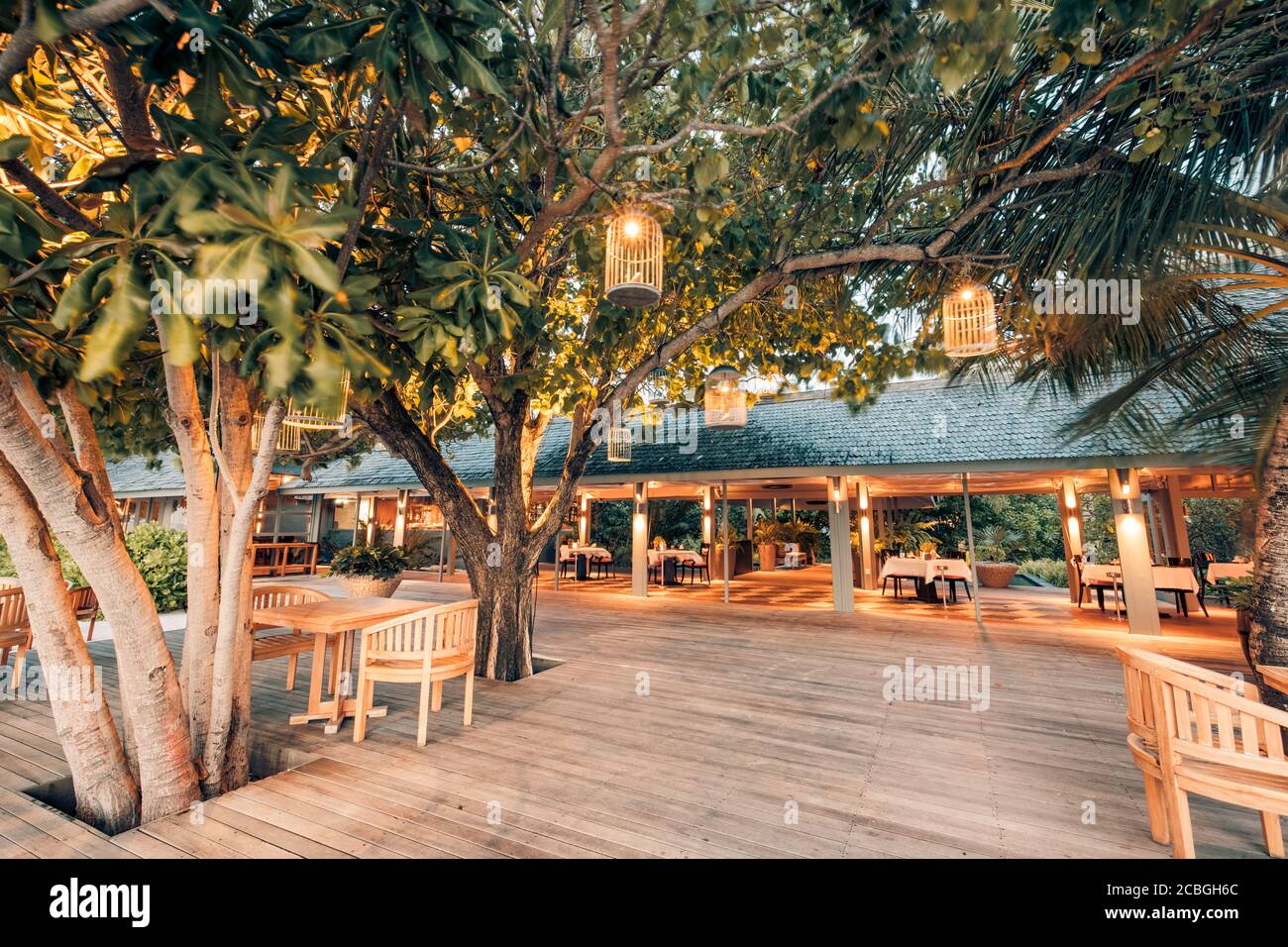Restaurant im Freien am Strand bei Sonnenuntergang, wunderschöne Aussicht auf das Restaurant im Freien und im Innenbereich bei Kerzenbeleuchtung, Holzterrasse mit Stühlen Stockfoto