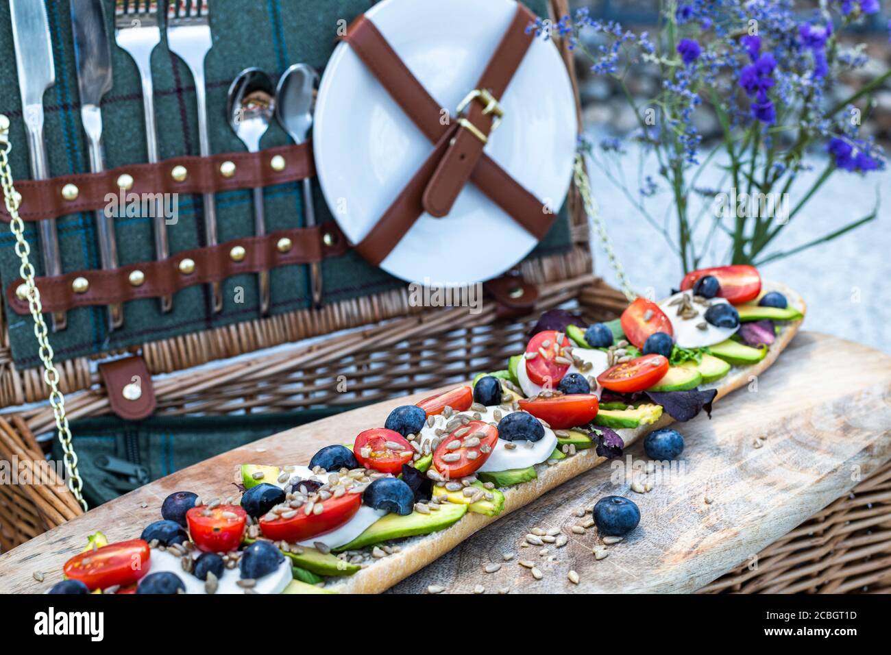 Stilvolles Picknick im Sommer mit Picknickkorb und vegetarischem Baguette mit Avocado, Tomaten und Mozarella-Käse Stockfoto