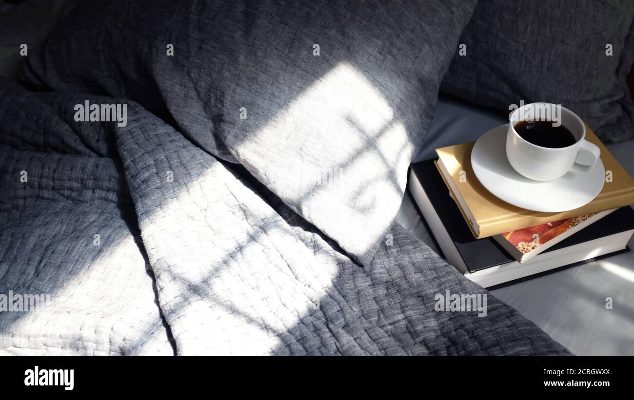 Morgenlicht auf grauem Bett mit einem Stapel Bücher Und eine Tasse frischen Kaffee Stockfoto