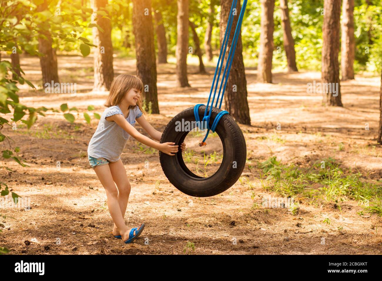Glücklich aktives Kind Mädchen spielen auf Schaukel Rad im Wald an sonnigen Sommertag. Sommer Aktivitäten im Freien für Kinder. Vorschulkind mit Spaß und Swingi Stockfoto