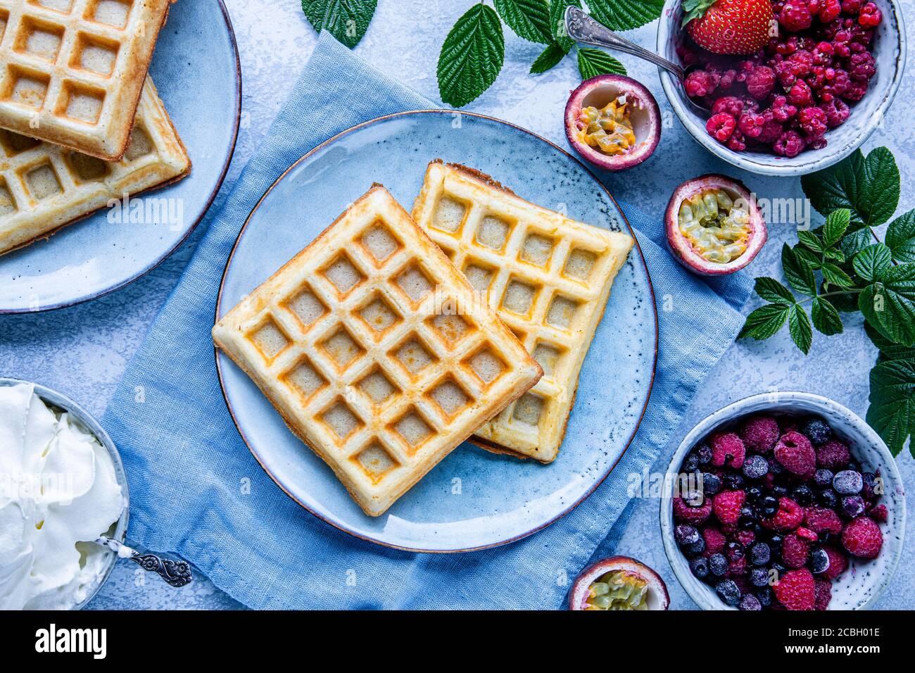 Belgische Waffeln mit Himbeeren, Blaubeeren und Passionsfrucht. Es gibt eine Schüssel Schlagsahne auf dem Tisch. Das Essen ist von oben gesehen, flach gelegt Stockfoto