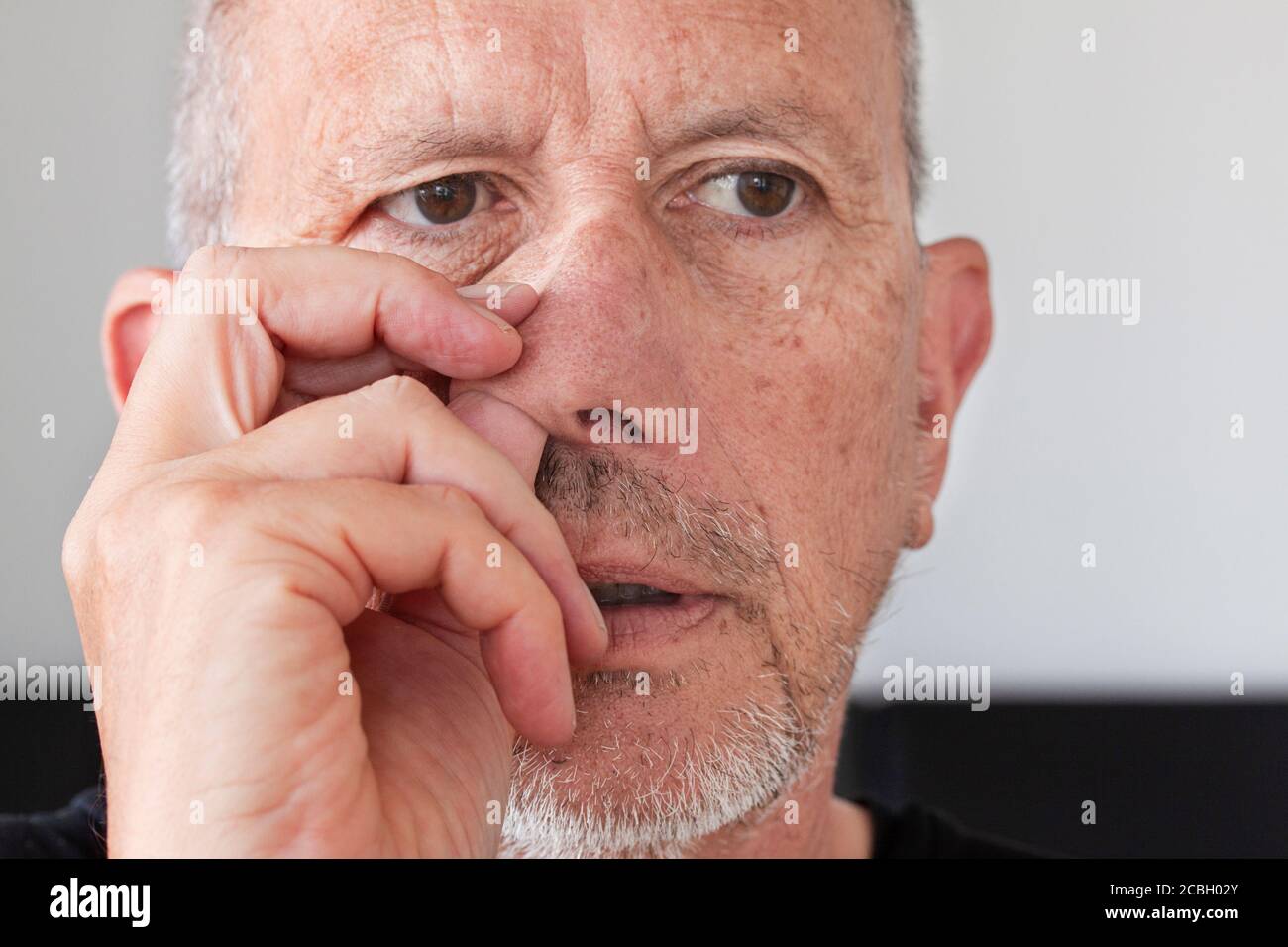 Älterer Mann mit unrasiertem Bartstoppel, der seine Nase pflückt. Daumen nach oben in seine Nase. Nahaufnahme des Bildes. Stockfoto