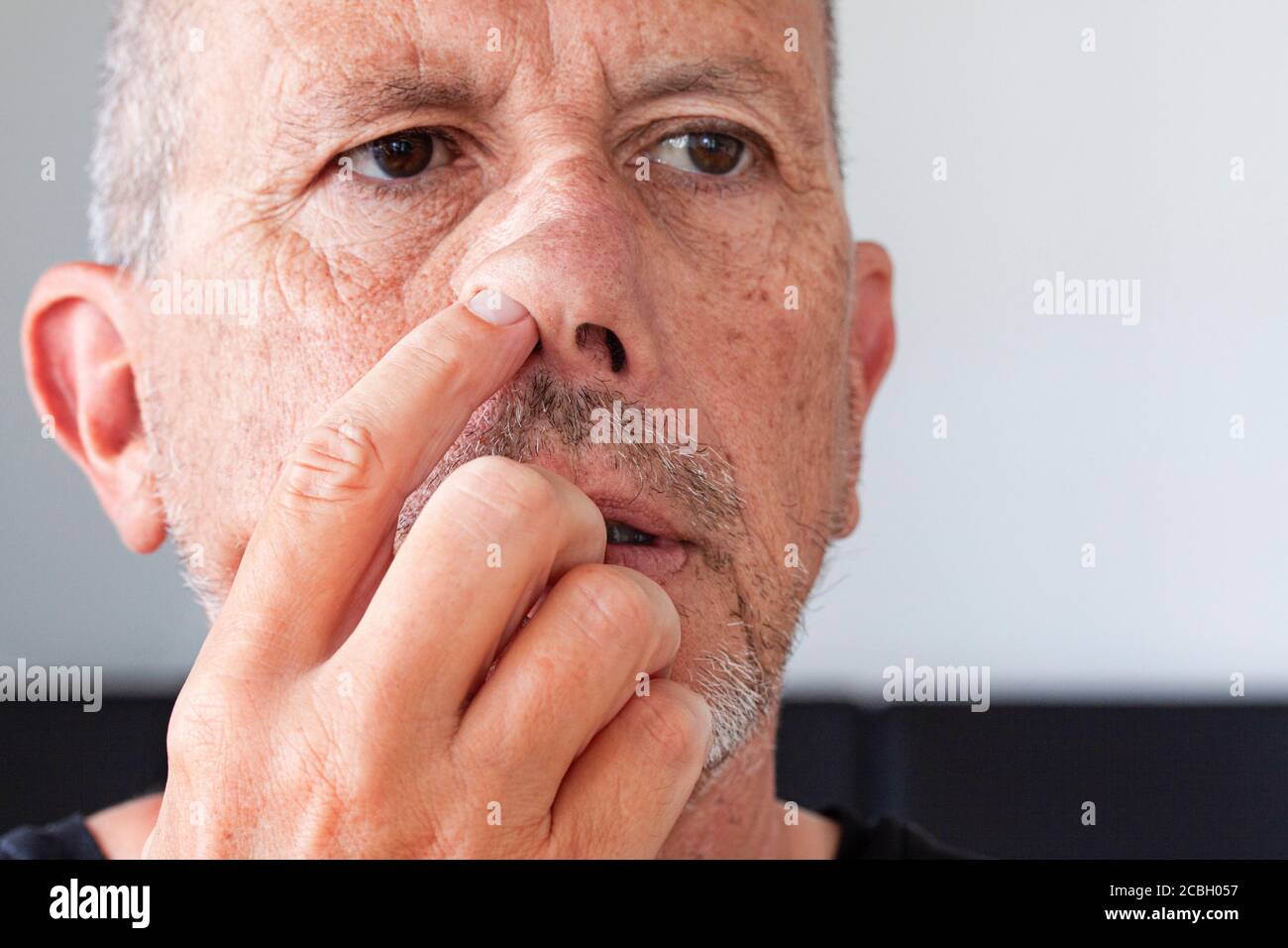 Älterer Mann mit unrasiertem Bartstoppel, der seine Nase pflückt. Zeigefinger nach oben in seine Nase. Nahaufnahme des Bildes. Stockfoto