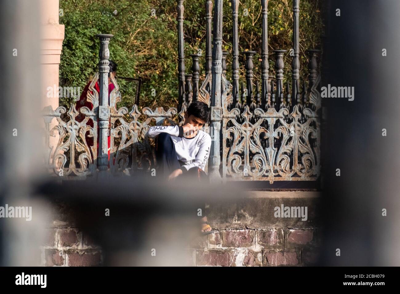 Bhopal, Madhya Pradesh, Indien - März 2019: Ein ehrliches Porträt eines jungen indischen Teenagers, der auf einer Wand sitzt und nachdenklich starrt. Stockfoto