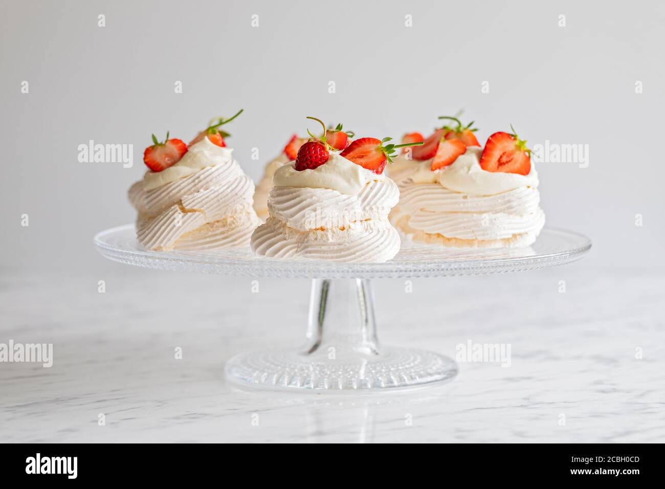 Mini Pavlova Meringue Nester mit Schlagsahne und hausgemachten frischen Bio-Erdbeeren. Die Mini-Baiser-Desserts werden auf einem Glas-Kuchen-Sta präsentiert Stockfoto