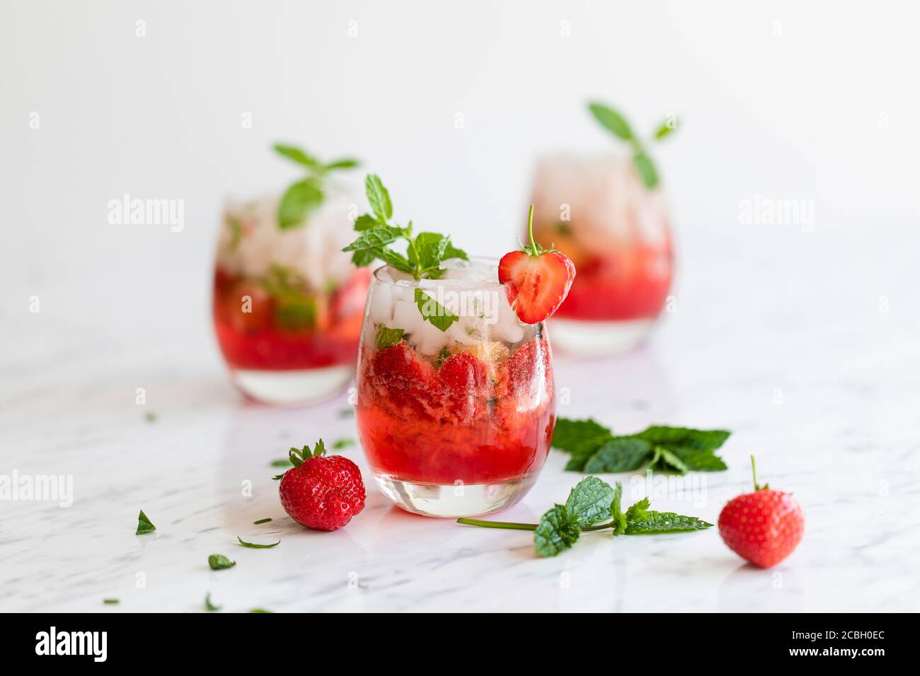 Frische Erdbeer Mojito Getränke. Es gibt drei Getränke auf dem weißen Marmortisch, und sie sind mit Erdbeeren und frischer Minze dekoriert. Es gibt s Stockfoto