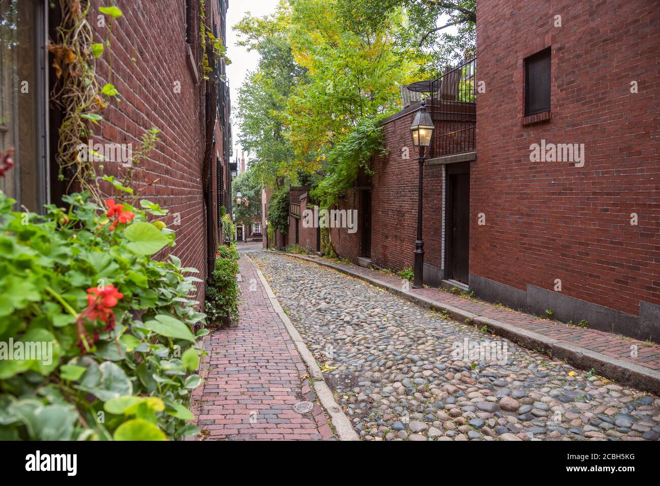 Schmale Gasse mit alten Backsteinhäusern und Gas gesäumt Beleuchtete Lampenpfosten an einem bewölkten Herbsttag Stockfoto