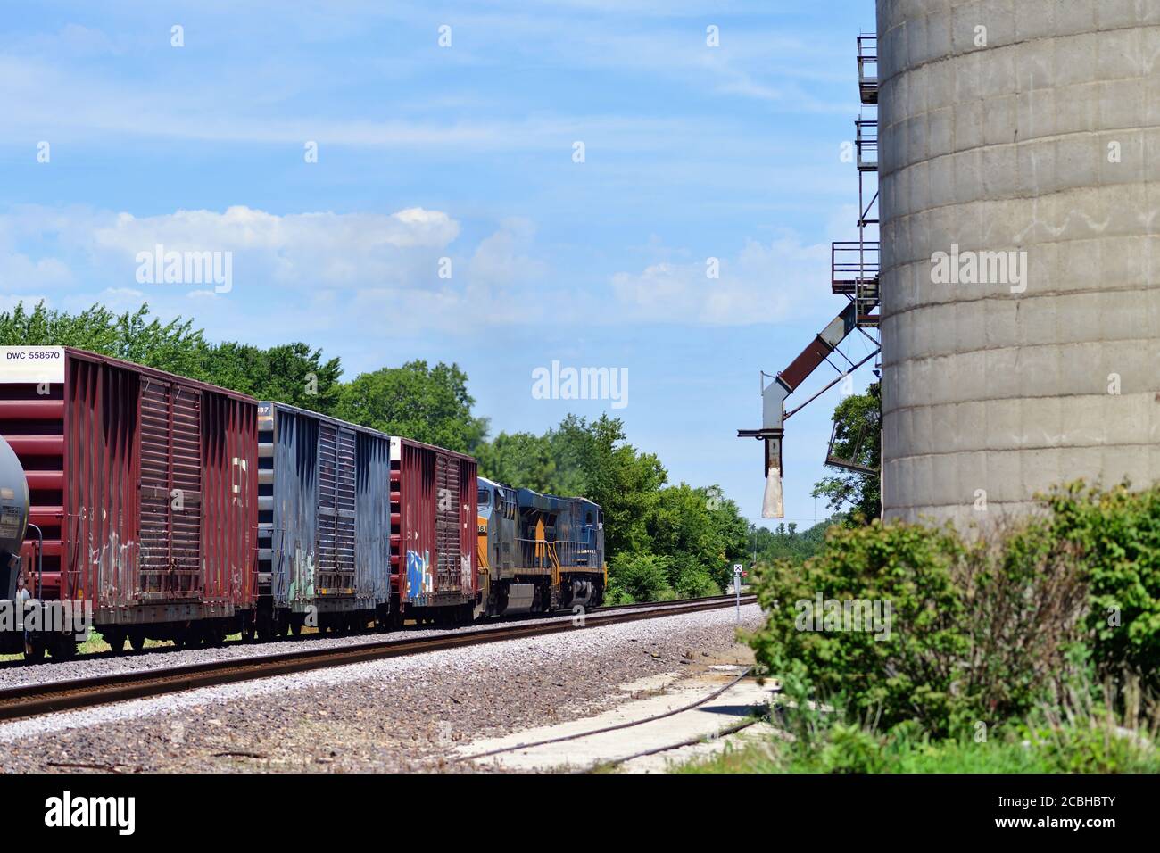 Watseka, Illinois, USA. Ein Paar Lokomotiven führen einen CSX Transportation Manifest Güterzug an einem Getreideaufzug in Wasteka, Illinois vorbei. Stockfoto