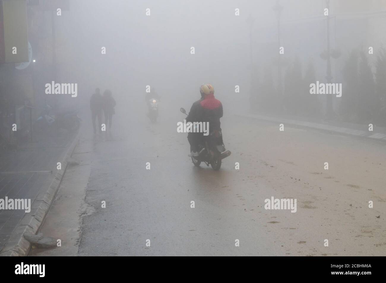 Ein Mann fährt mit seinem Motorrad durch dichten Nebel in der Stadt. Stockfoto