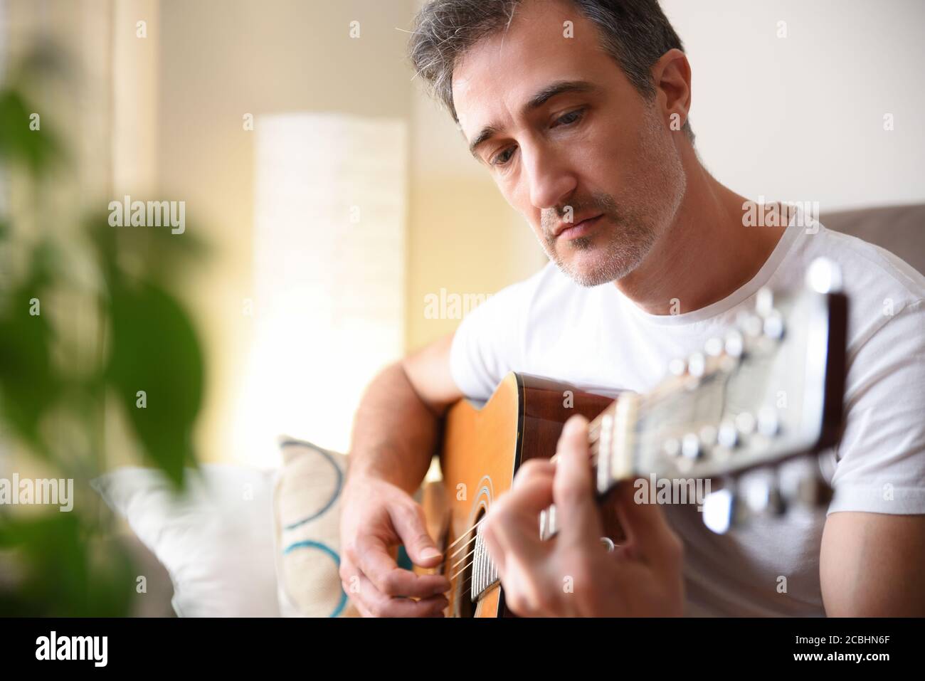 Detail des Mannes spielt akustische Gitarre mit weißen kurzen Ärmeln shirt im Wohnzimmer zu Hause Stockfoto