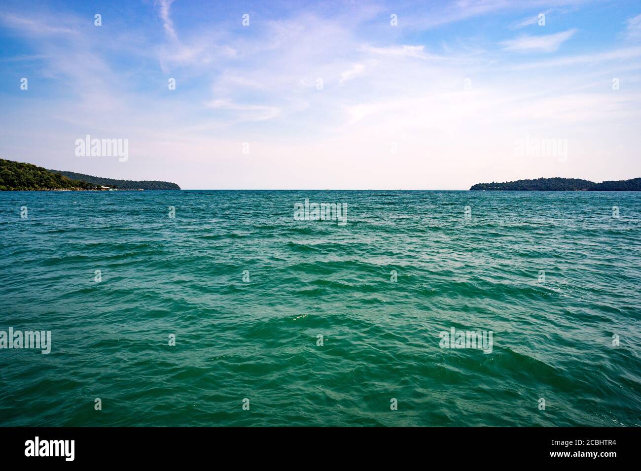 Türkisfarbenes Wasser im Südchinesischen Meer. Die Horizontlinie zwischen Meer und blauem Himmel mit Wolken. Kleine Inseln im Hintergrund. Stockfoto