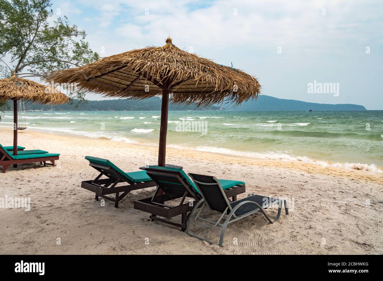 Ruhige Strandszene mit Sonnenliegen und Strohschirmen unter Kokospalmen in der Nähe des karibischen Meeres. Tropisches Paradies mit Liegestühlen auf weißem Sand, nein Stockfoto