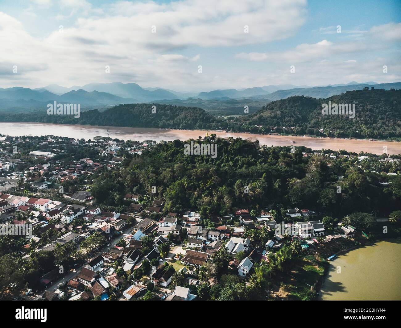 Luang Prabang, Laos. Luftaufnahme der Stadt Luang Prabang in Laos. Wolkiger Himmel über einer kleinen Stadt, umgeben von Bergen. Autoverkehr und Fluss Stockfoto