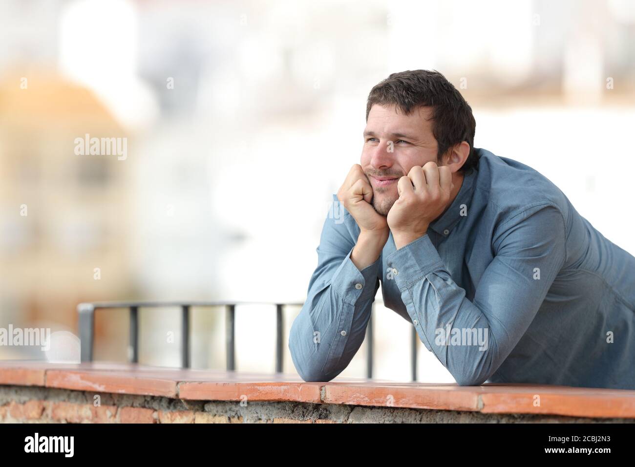 Nachdenklicher Mann, der auf einem Balkon auf einem nachdenklichen Stadt Stockfoto