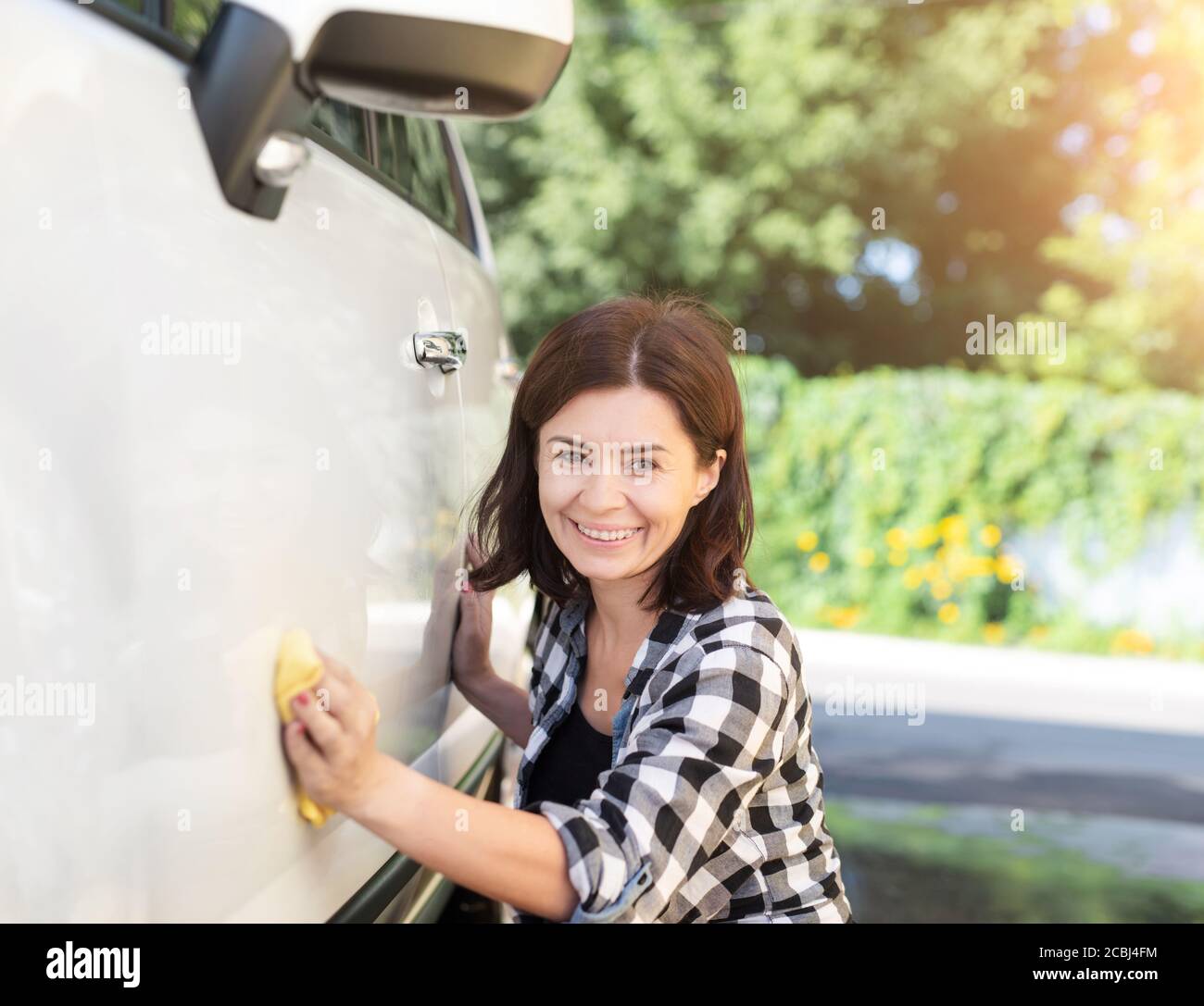 Glückliche Frau mit Lappen neben weiß glänzendem Auto auf Sonniger Tag Stockfoto