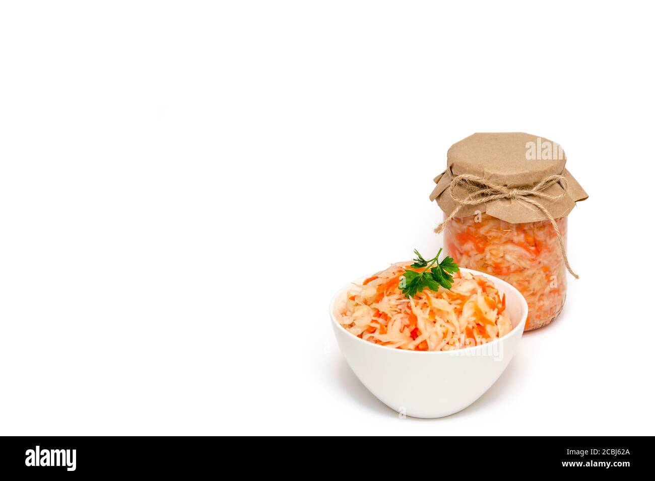 Hausgemachtes Sauerkraut mit Karotte in weißer Keramikschale und einem Glas auf weißem Hintergrund. Fermentierte Lebensmittel. Gesunde Ernährung und Diät-Konzept. Nahaufnahme Stockfoto