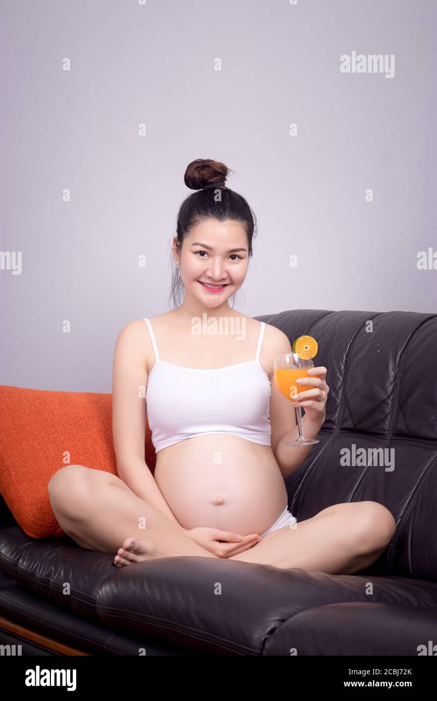 Schwangere Frau Essen Lebensmittel mit Zutat für gesunde Konzept : Asian junge schwangere Frau halten frischen Orangensaft im Glas mit lächelnfreundlichen Gesicht Stockfoto