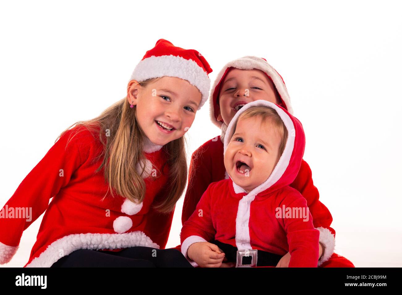 3 Kinder, 2 Jungen (1 Jahr - 4 Jahre) 1 Mädchen (6 Jahre) sitzt zusammen auf dem Boden in Weihnachtsmann Kostüm lachend. Isoliert auf weiß Stockfoto