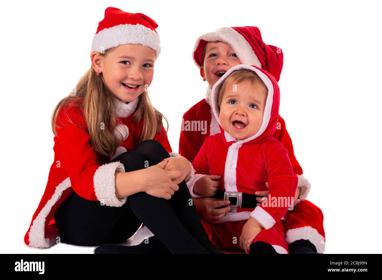 3 kleine Kinder, 2 Jungen (1 Jahr - 4 Jahre) 1 Mädchen (6 Jahre) sitzt zusammen auf dem Boden in einem Weihnachtsmann Kostüm lächelnd. Isoliert Stockfoto