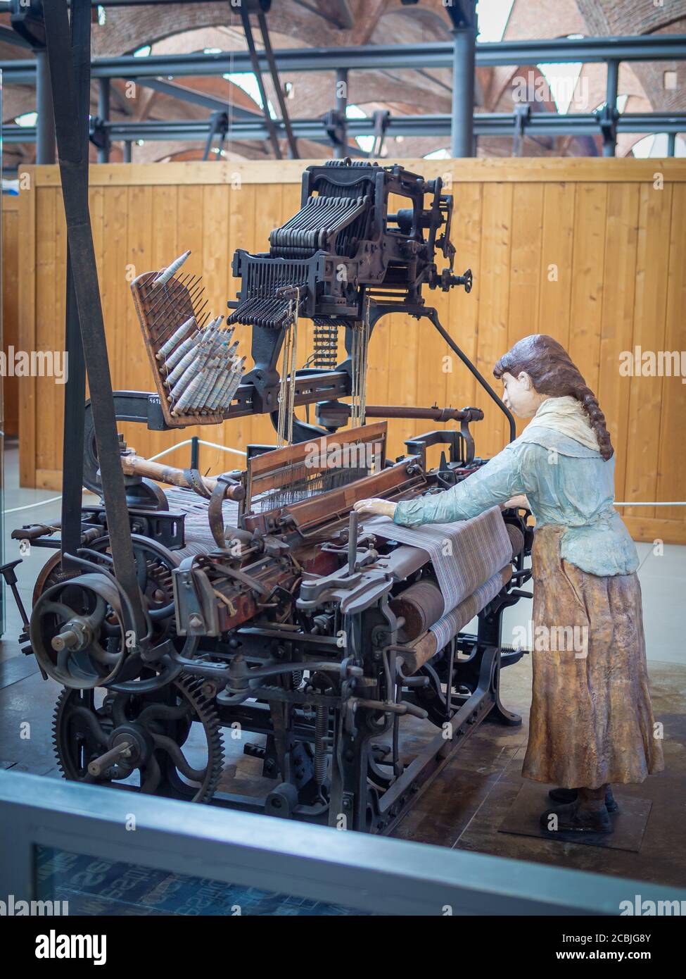 Steinfigur einer Arbeiterin bei der Arbeit in einer Textilfabrik, die an einer echten Baumwollmaschine (Loom) arbeitet. Stockfoto