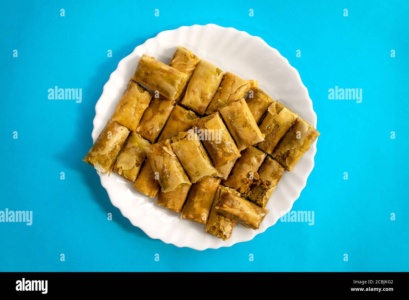 Traditionelle türkische, arabische, mittelöstliche Baklava. Draufsicht. Arabisch gebackene Süßigkeiten in weißem Teller auf blauem hellen Hintergrund. Mini Baklawa Stockfoto
