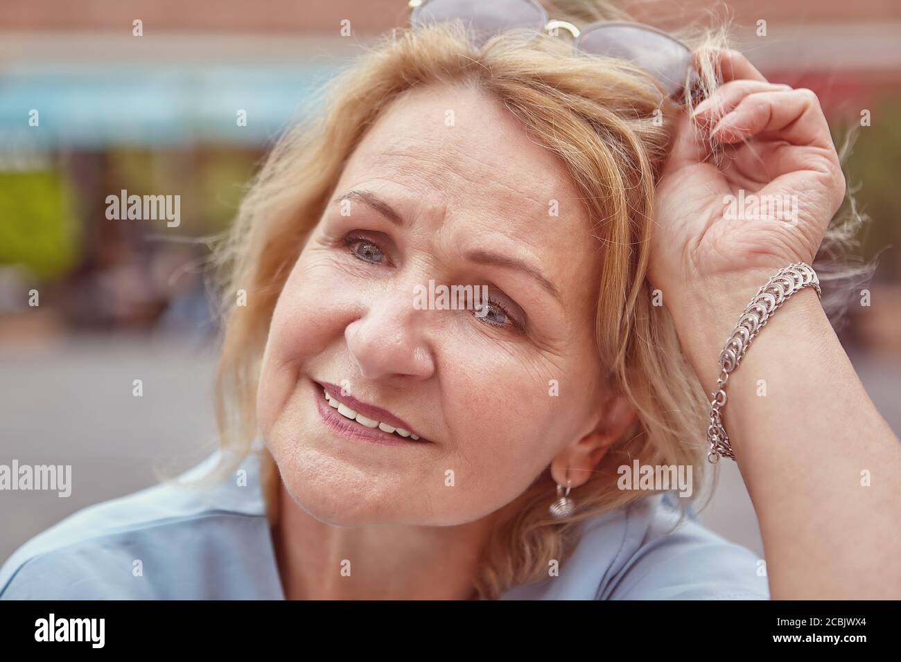 Porträt der charmanten kaukasischen Senior Dame über 60 Jahre alt mit blonden Haaren und Sonnenbrille. Weiß Attraktive ältere lächelnde Frau ist zu Fuß in der Kneipe Stockfoto