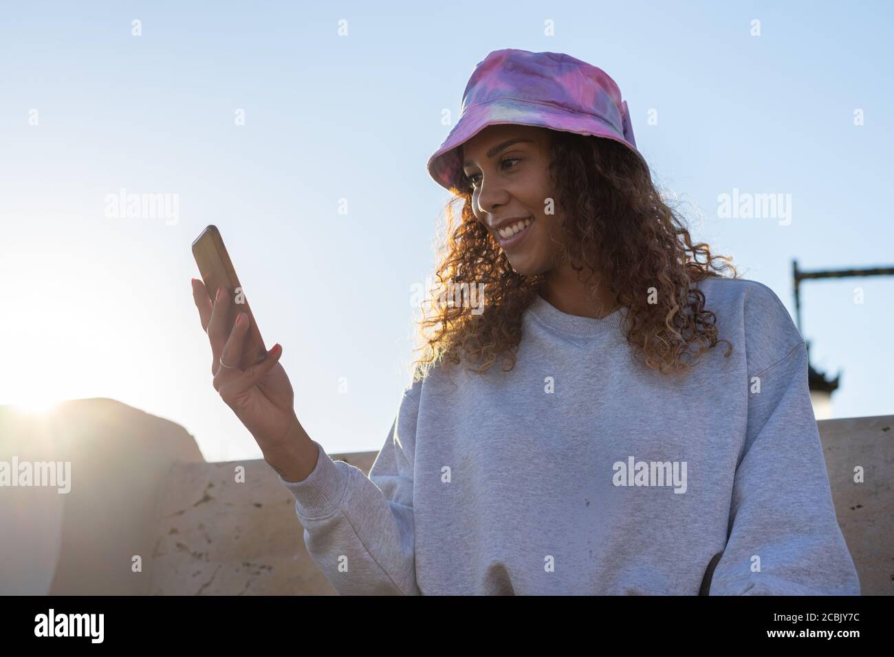 Portrait einer attraktiven jungen schwarzen Frau, die mit dem Handy im Freien sitzt und mit der Maske abschaltet. Konzeptkommunikation Stockfoto