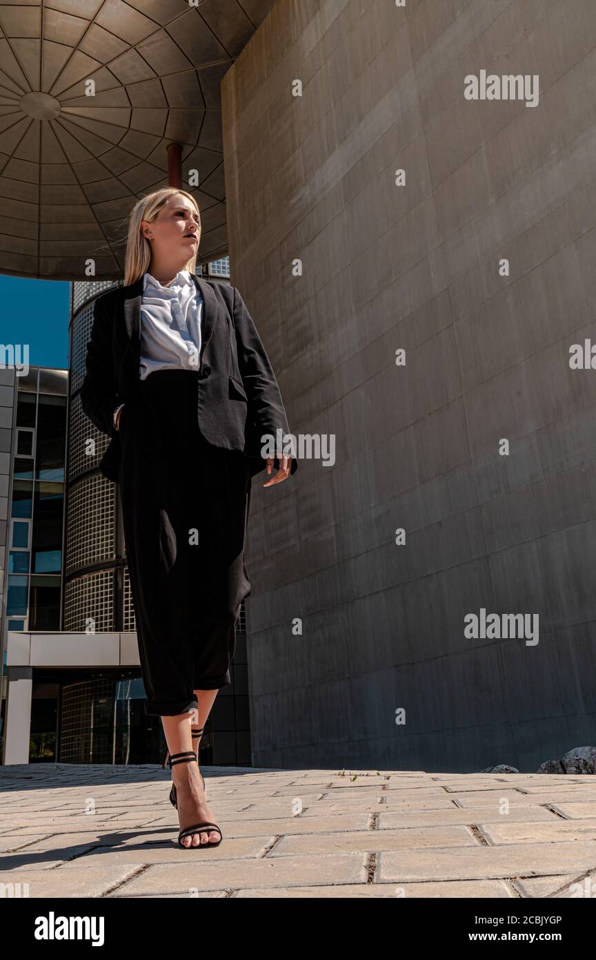 Eine vertikale Aufnahme einer jungen blonden Geschäftsfrau in Formelle Kleidung zu Fuß in der Nähe des Gebäudes Stockfoto