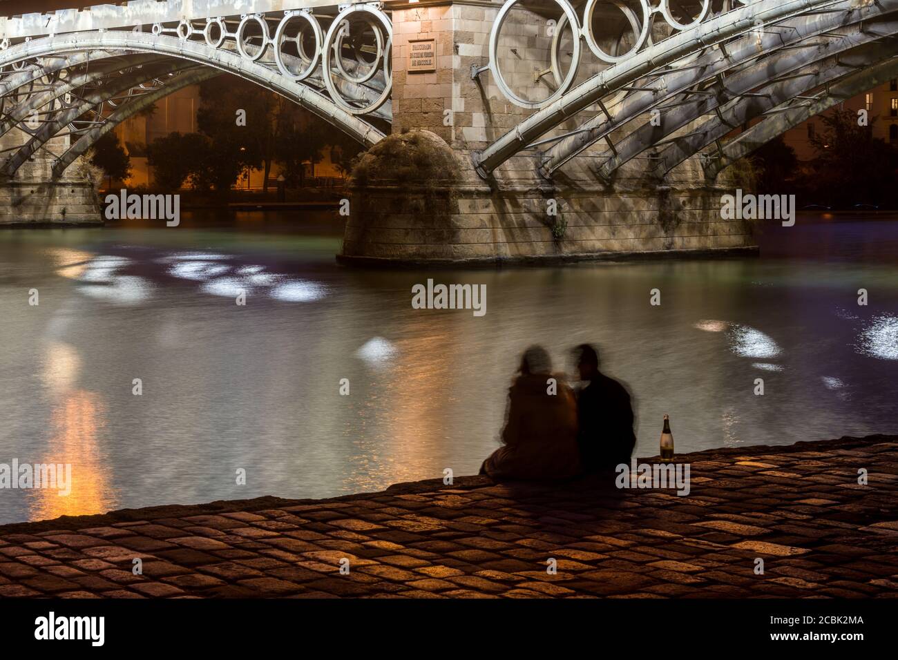 Junges Paar, das am Guadalquivir-Fluss und an der Triana-Brücke Sekt trinkt, Sevilla, Spanien Stockfoto