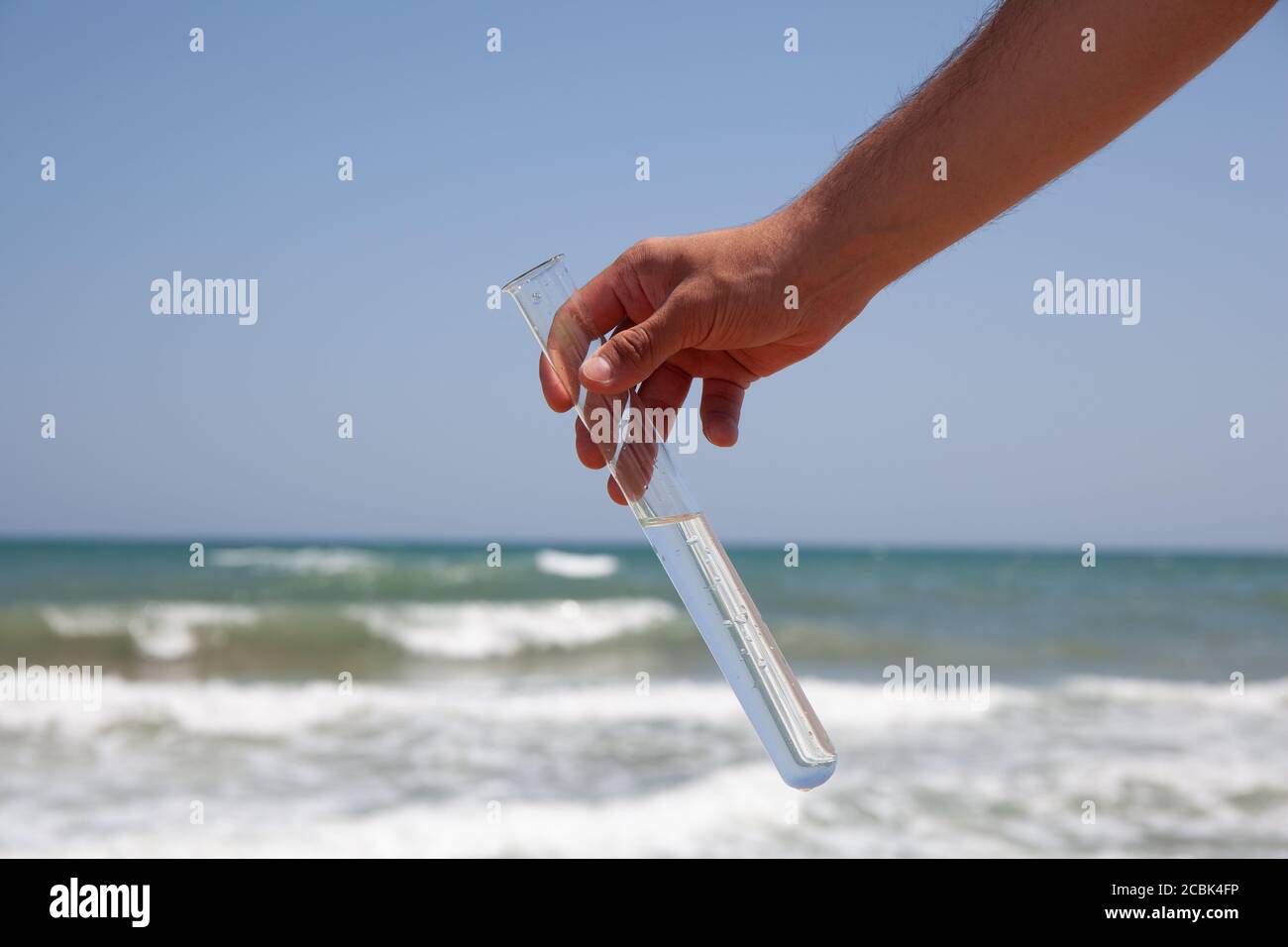 Reagenzglas mit sauberem Meerwasser in einer Hand auf Ein Meereshintergrund während ökologischer Prüfung Stockfoto